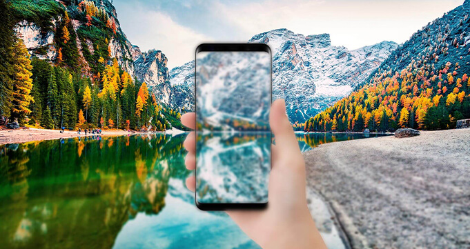 a hand holding a cell phone with view of mountains
